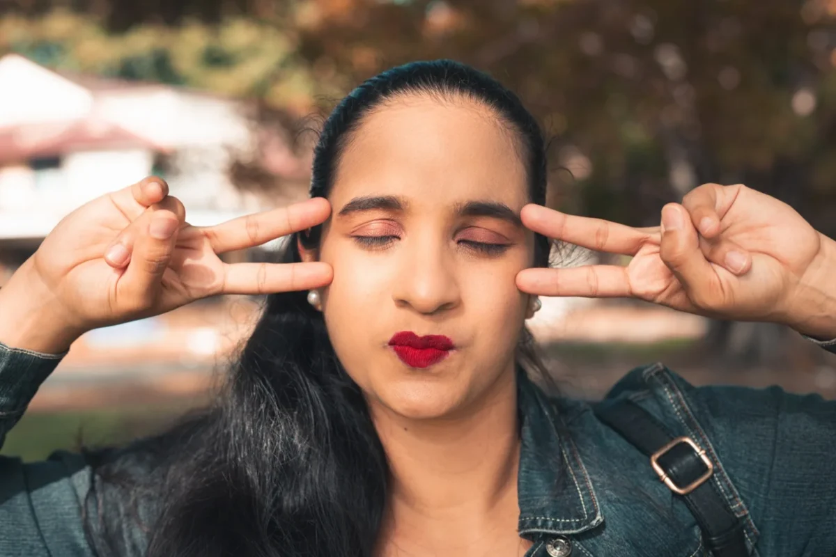 woman with eyes closed making peace signs with hands