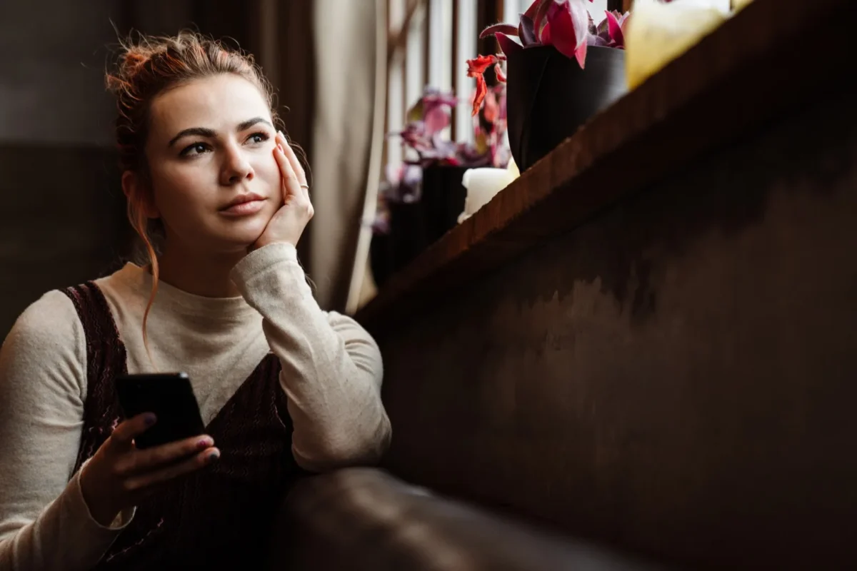 woman holding phone looking into distance thoughtfully