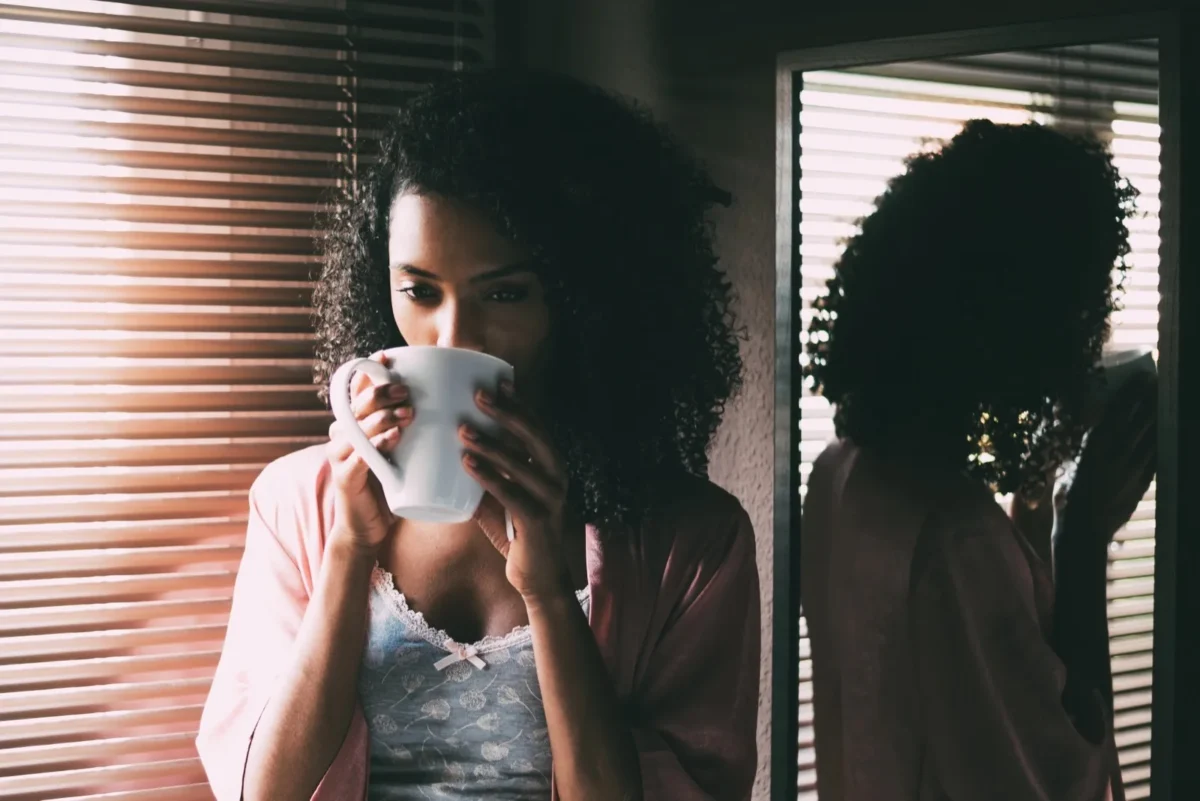 woman standing by window drinking coffee
