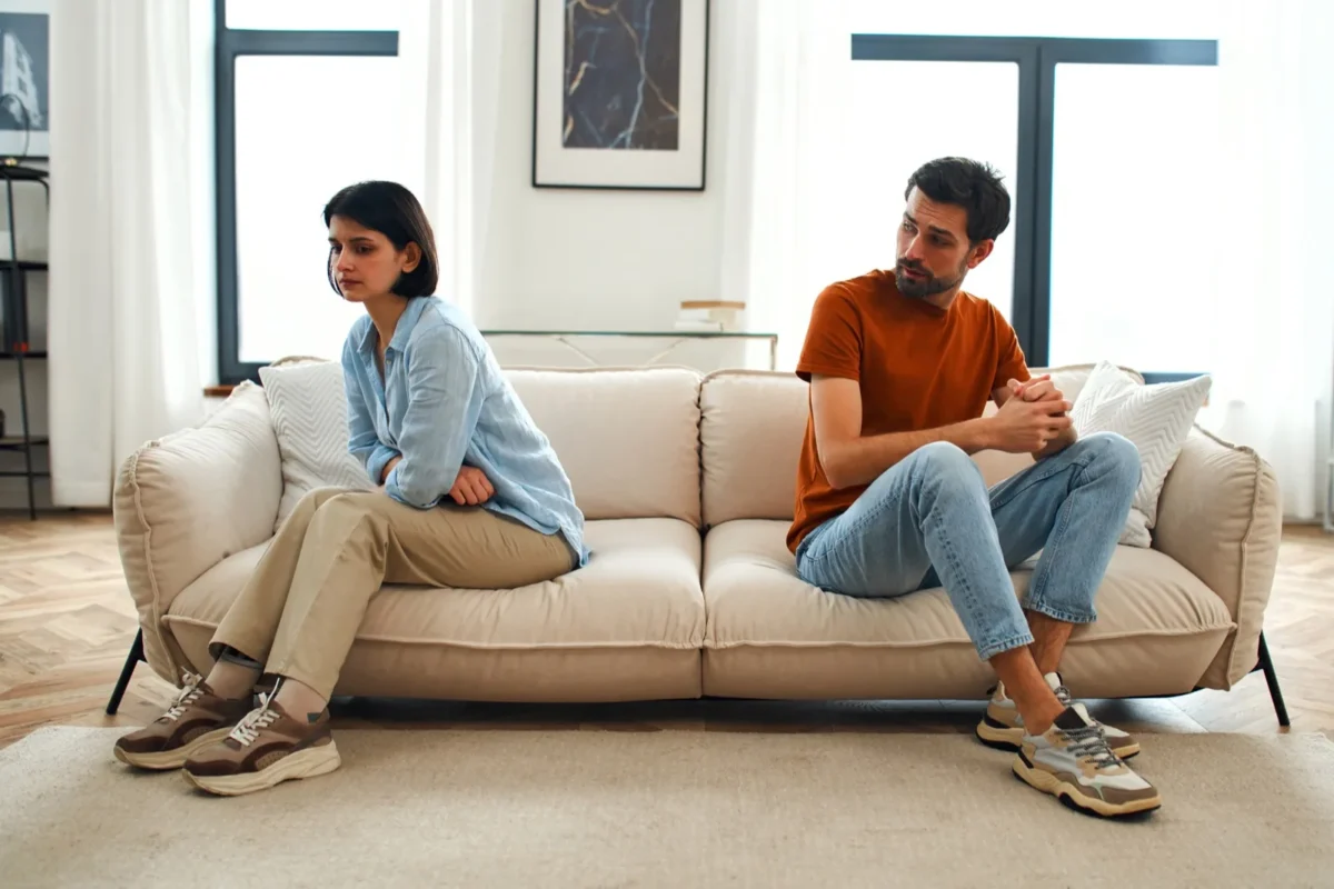 couple sitting apart on sofa trying to understand each other