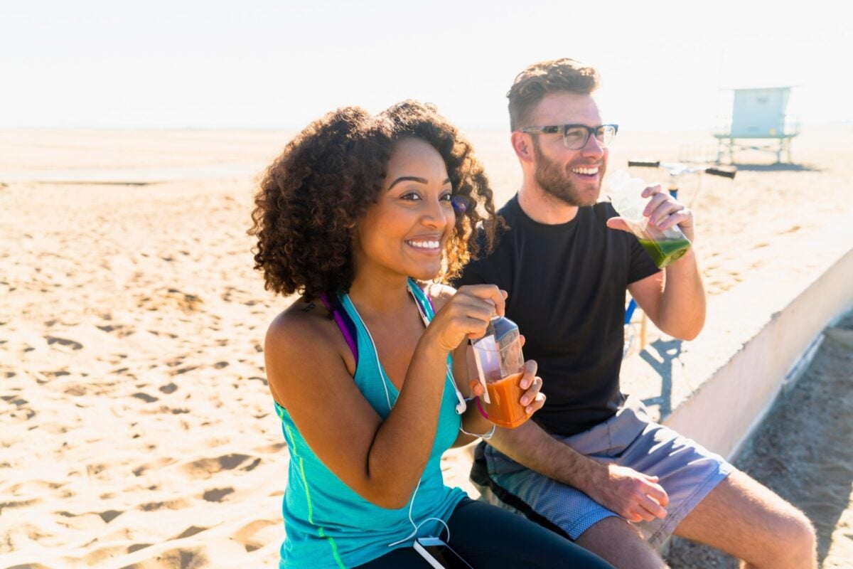 couple having smoothies on beach after workout