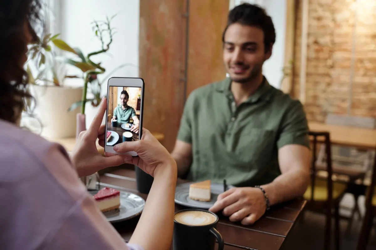 woman taking phone photo of man in cafe