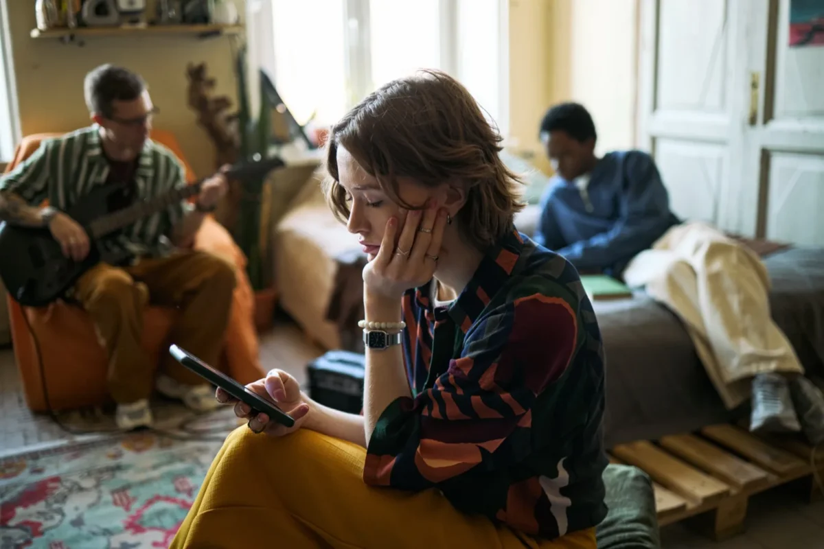 woman sitting away from group looking at phone